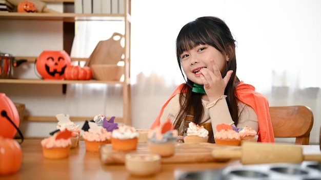 Carina ragazza asiatica in costume di Halloween che assaggia un cupcake di Halloween in cucina