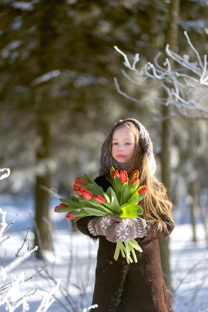 Carina ragazza caucasica che indossa guanti di lana con cappotto caldo e uno scialle che tiene un mazzo di tulipani in una fredda giornata invernale