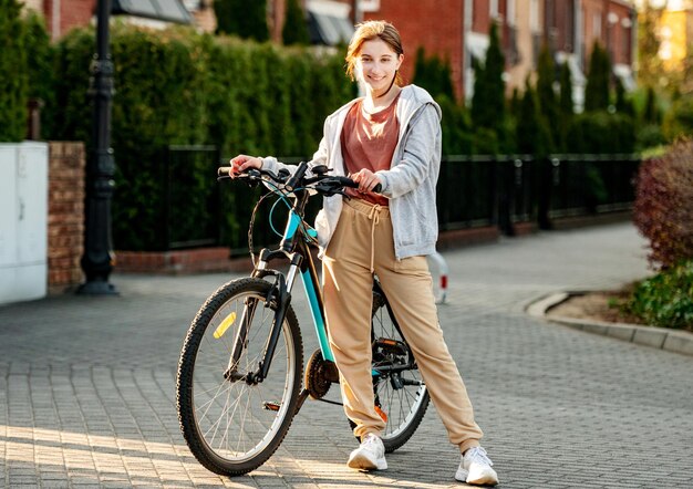 Carina ragazza che ride in piedi con una bicicletta la sera in una città tranquilla