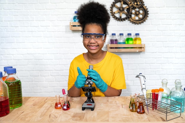 Carina ragazza con capelli afro e ragazzo studia la scienza con il microscopio e la sostanza chimica di prova