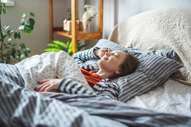 Carina ragazza felice che dorme e si sveglia in una mattina di sole e nel suo letto accogliente