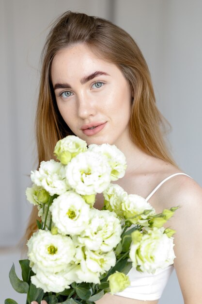 Carina ragazza felice in maglietta bianca bianca, con in mano un bouquet e guarda i fiori, godendosi l'odore. bella ragazza teenager bionda con le parentesi graffe sui denti che sorride?