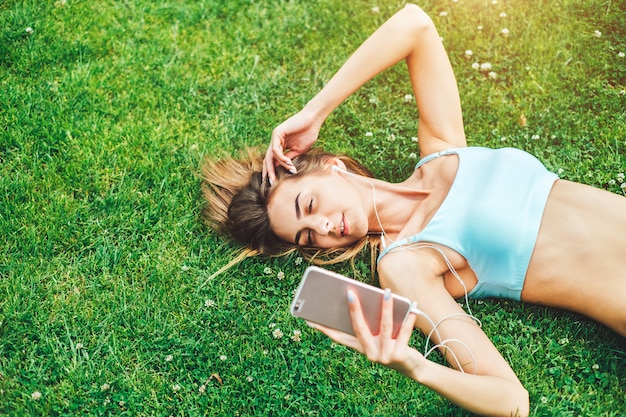 Carina ragazza sportiva con telefono rilassante all&#39;aperto dopo l&#39;allenamento