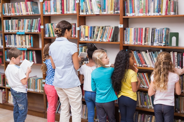 Carino alunni e insegnante alla ricerca di libri in biblioteca