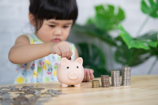 Carino asia bambina goccia monete nel salvadanaio, concetto di risparmio.