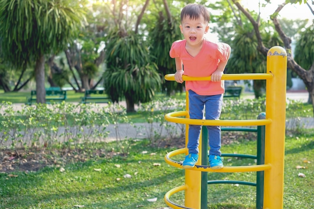 Carino asiatico 3 anni bambino bambino bambino divertirsi provando a arrampicarsi sulla struttura rampicante al parco giochi all'aperto