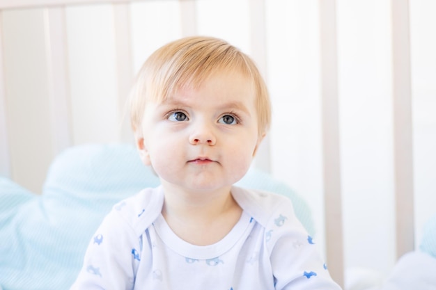 Carino bambino biondo con occhi grandi primo piano o ritratto nella culla a casa il concetto di prodotti per bambini e accessori