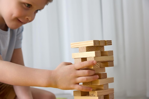 Carino bambino caucasico smonta diligentemente una torre fatta di barre di legno