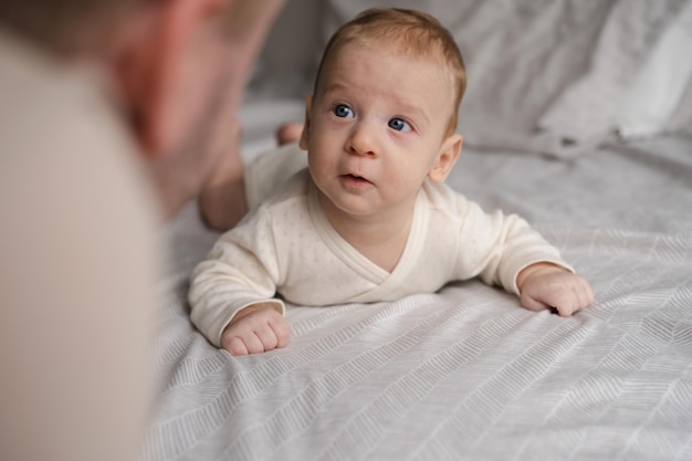 Carino bambino di due o tre mesi che guarda il suo genitore o adulto sdraiato sulla pancia nello spazio della copia del letto