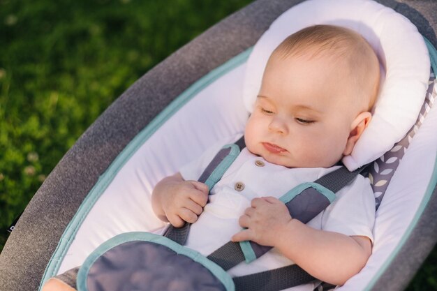 Carino bambino felice seduto su una sedia sull'erba all'aperto in estate