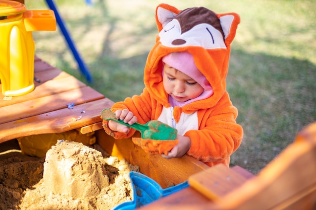 carino bambino in tuta arancione gioca nella sabbia nella sandbox all'aperto in una giornata di sole