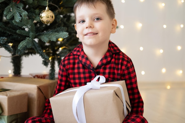 carino bambino ragazzo in pigiama rosso con scatole regalo seduto sotto l'albero di natale a casa