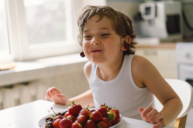 Carino bel ragazzino che mangia ciliegia fresca e fragola Cibo sano infanzia e sviluppo