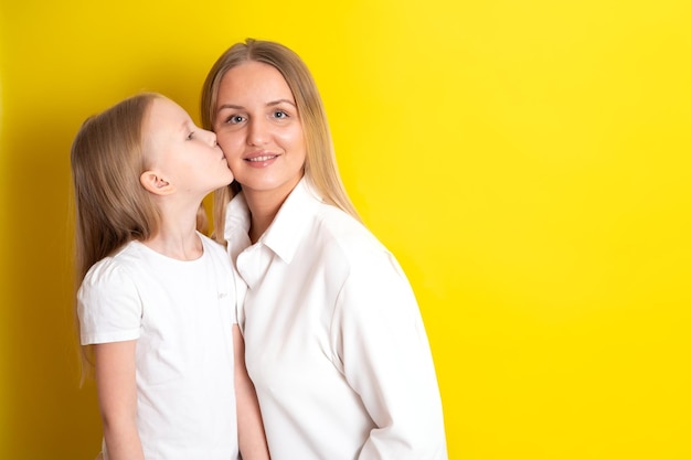 Carino bella madre e figlia in abiti bianchi Abbracciare la famiglia Sfondo giallo posto per il testo Foto di alta qualità