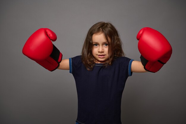 Carino caucasica bambina indossa guanti da boxe rossi pone contro il muro grigio Sfondo con copia spazio per la pubblicità per il Boxing Day