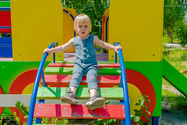 Carino divertente biondo piccolo bambino bambino ragazzo bambino che scende la scaletta di legno nel parco giochi per bambini lo sviluppo fisico-emotivo e l'asilo nido d'infanzia concetto di asilo nido in estate