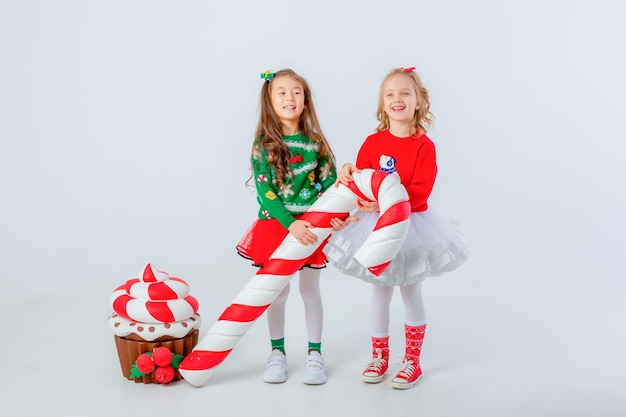 Carino due bambine in maglione rosso, confezione regalo seduta su sfondo bianco Spazio del testo del concetto di Natale