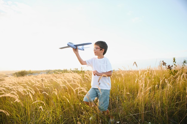 Carino felice allegro bambino che corre velocemente lungo la collina erbosa in campagna tenendo in mano un grande aereo giocattolo Ragazzo che gioca durante l'ora del tramonto in serata Fotografia a colori orizzontale