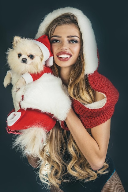 Carino felice Natale donna in guanti di pelliccia bianca con cane - isolato su sfondo nero. Natale, Capodanno e festa. La ragazza ed il cane attraenti sono vestiti in cappello rosso della Santa. Anno del cane.