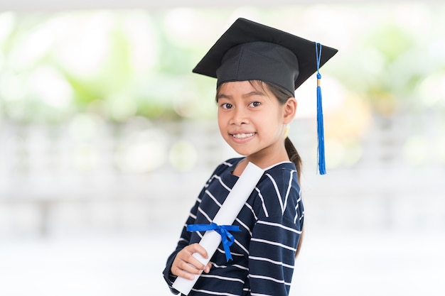 Carino felice ragazzo asiatico diplomato con cappello di laurea e un diploma isolato su sfondo bianco