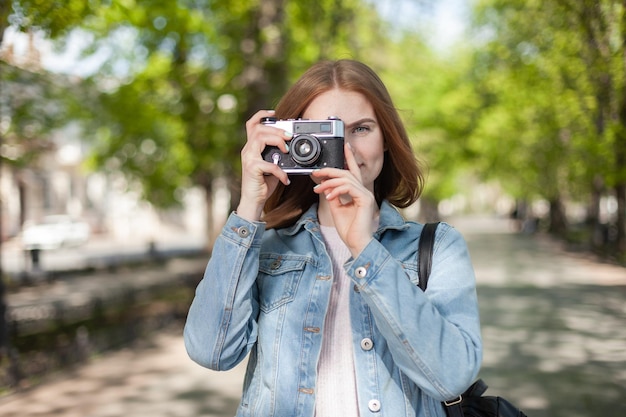 Carino giovane donna attraente turista in giacca di jeans con fotocamera retrò in città