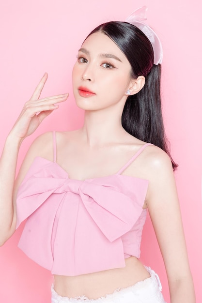 Carino modello di donna asiatica riuniti in coda di cavallo con stile trucco coreano sul viso hanno labbra carnose e pelle pulita e fresca indossando canotta rosa su sfondo rosa isolato