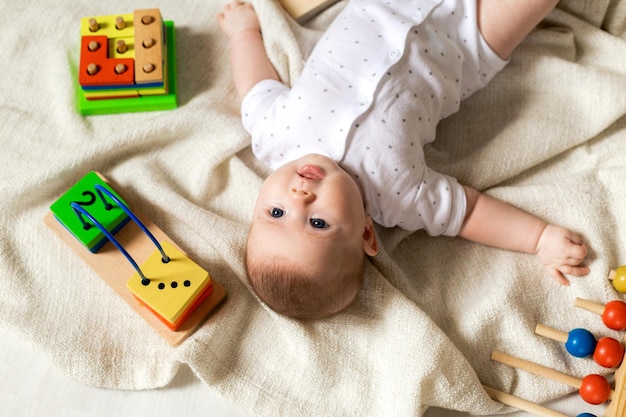 Carino neonato sta giocando con giocattoli educativi sdraiati sul pavimento su una coperta di lino grigio