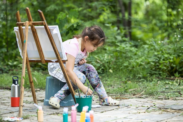 Carino piccolo artista pittura immagine pittura su tela nella foresta della natura Bambina felice in giardino