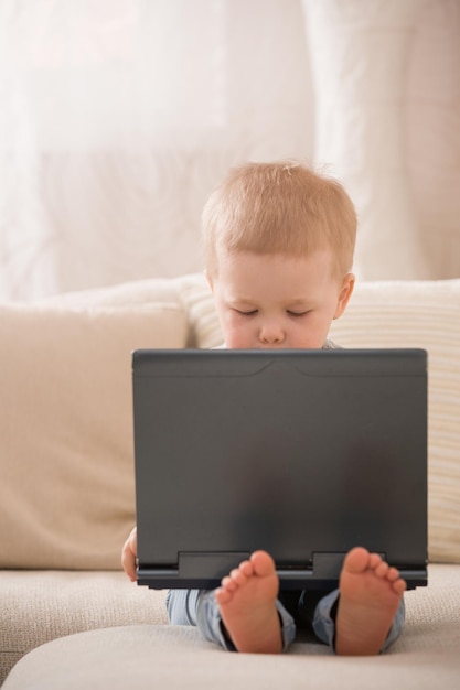 Carino piccolo ragazzo seduto sul divano con il suo computer portatile e guardando la finestra