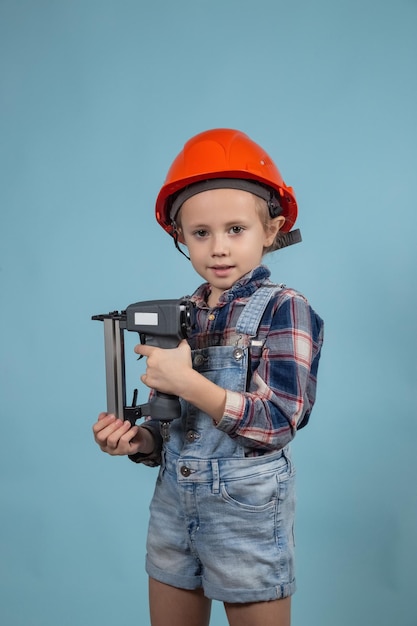 Carino ragazzino caucasico indossa un casco di sicurezza arancione, tenendo a portata di mano una cucitrice meccanica. Concetto di costruzione e riparazione.