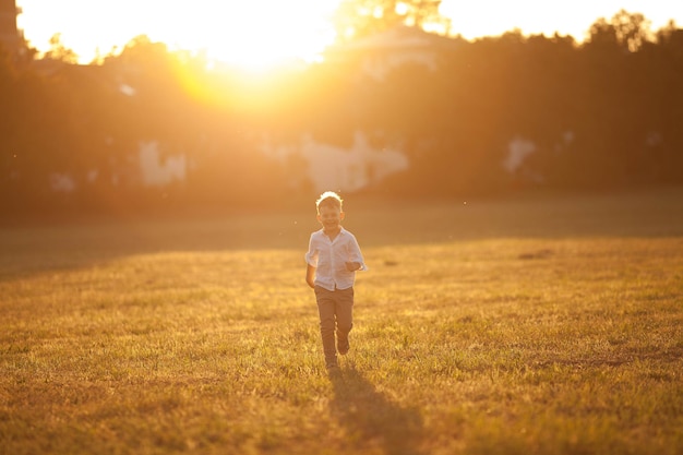 Carino ragazzo biondo di 5 anni in abiti semplici e leggeri corre al tramonto in un campo al sole Bambino felice Sera d'estate Tramonto