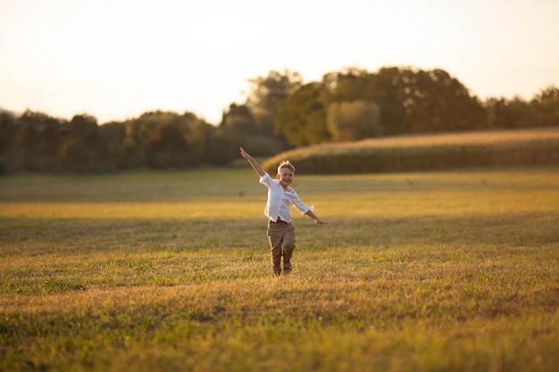 Carino ragazzo biondo di 5 anni in abiti semplici e leggeri corre al tramonto in un campo al sole Bambino felice Sera d'estate Tramonto