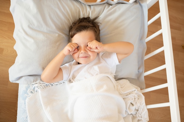 Carino ragazzo caucasico strofinandosi gli occhi al mattino sul letto. Foto di alta qualità