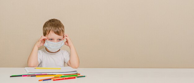 Carino ragazzo di 4 anni in maschera medica è seduto a casa in quarantena. Animazione per il bambino durante la quarantena - disegno.