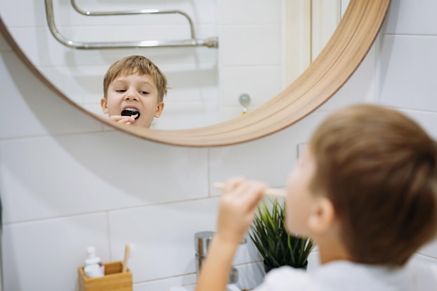 Carino ragazzo di 5 anni lavarsi i denti con spazzolino da denti di bambù in bagno Immagine con messa a fuoco selettiva