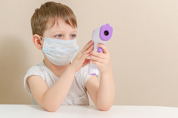 Carino ragazzo di quattro anni in una maschera medica interpreta un medico e misura la temperatura