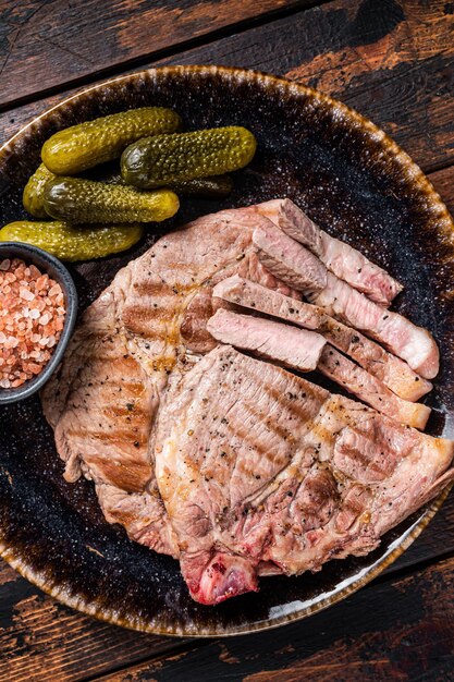 Carne alla griglia - Bistecche di maiale dalla carne del filetto del collo in piatto con i cetrioli sottaceto. Fondo in legno. Vista dall'alto.