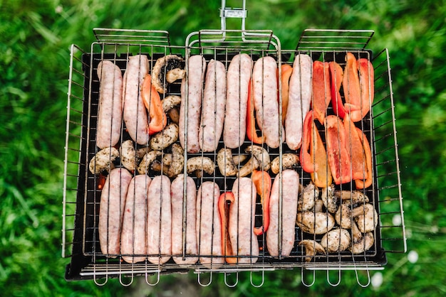 Carne alla griglia e salsicce con verdure e spezie su un braciere Vista dall'alto Deliziosa carne alla griglia assortita sulla griglia del barbecue con fumo e fiamme nell'erba verde