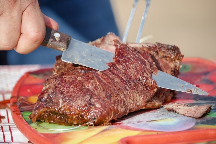 Foto carne arrosto e tagliata sul tavolo e fuoco di bivacco con legna da ardere in stile gaucho