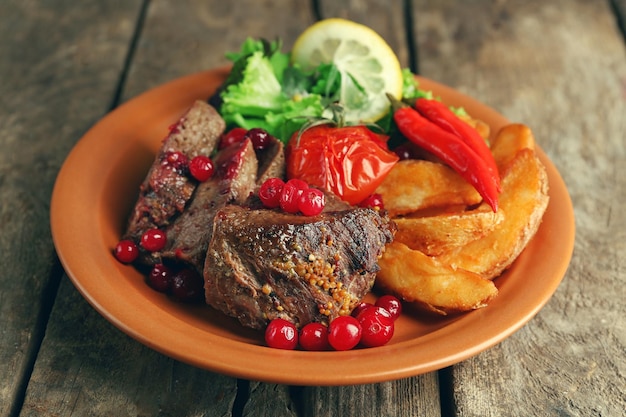 Carne arrosto saporita con insalata di salsa di mirtilli e verdure arrostite sul piatto su fondo di legno