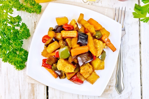 Carne arrosto, zucchine, melanzane, carote e peperoni dolci con miele, salsa di soia e vino rosso in un piatto su un tovagliolo sullo sfondo delle assi di legno in cima