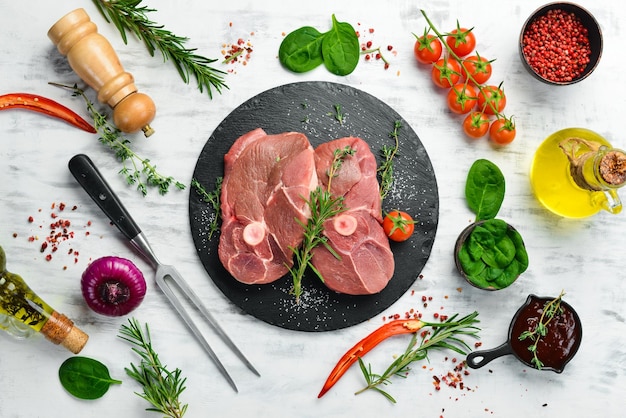 Carne Bistecca di agnello disossata cruda con rosmarino e spezie su uno sfondo di legno bianco Vista dall'alto