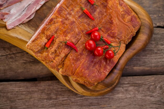 Carne con peperoni e pomodori. Pancetta cruda su tavola di legno. Il buongustaio ha cucinato il manzo. Piatto dal gusto piccante.