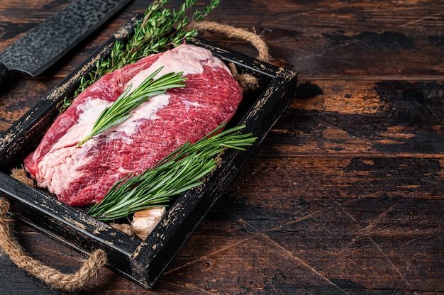 Carne cruda del manzo del petto tagliata su un vassoio di legno con il coltello. Fondo in legno scuro. Vista dall'alto. Copia spazio.