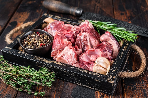 Carne cruda di agnello o capra tagliata a dadini per spezzatino con osso. Fondo in legno scuro. Vista dall'alto.