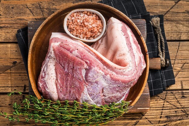 Carne cruda di pancia di maiale arrotolata in un piatto di legno con timo Sfondo in legno Vista dall'alto