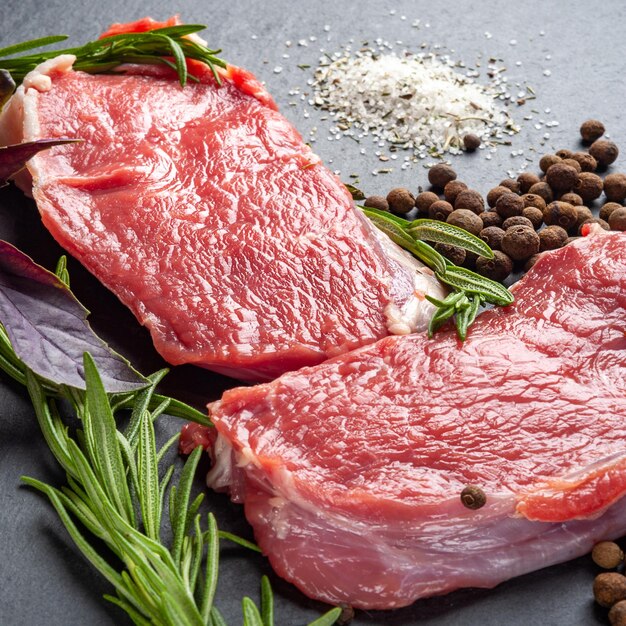 Carne cruda Due fette di carne cruda fresca sale pepe e rosmarino su una lastra di pietra ardesia nera