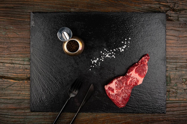 Carne cruda e coltello da forchetta e sale e pepe su una lastra di pietra nera