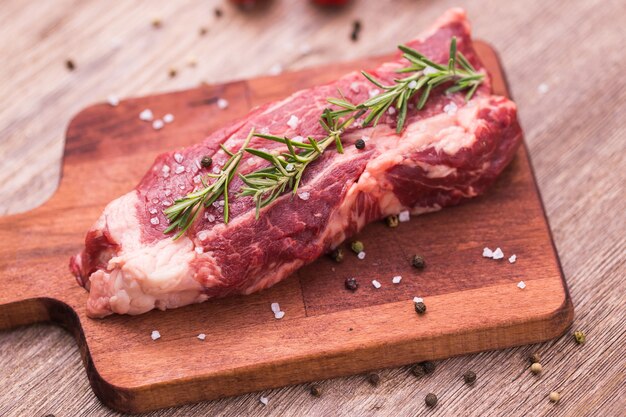 Carne cruda. Un grosso pezzo di braciola di manzo su un tagliere di legno con rosmarino e spezie.