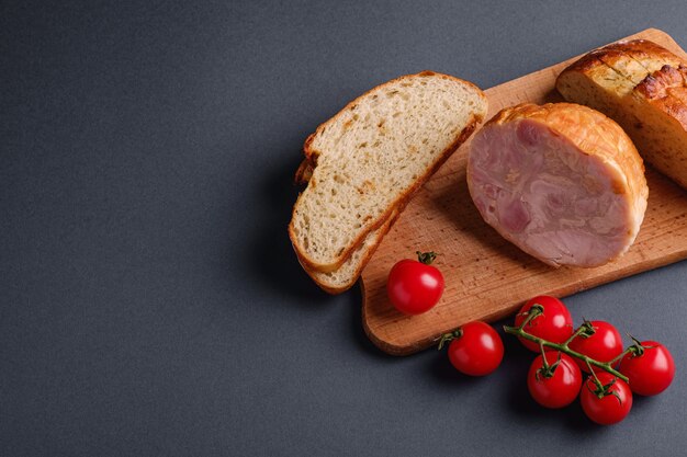 Carne del prosciutto di tacchino, ramo fresco dei pomodori ciliegia e pane affettato pagnotta sul tagliere di legno, tavola minima grigia